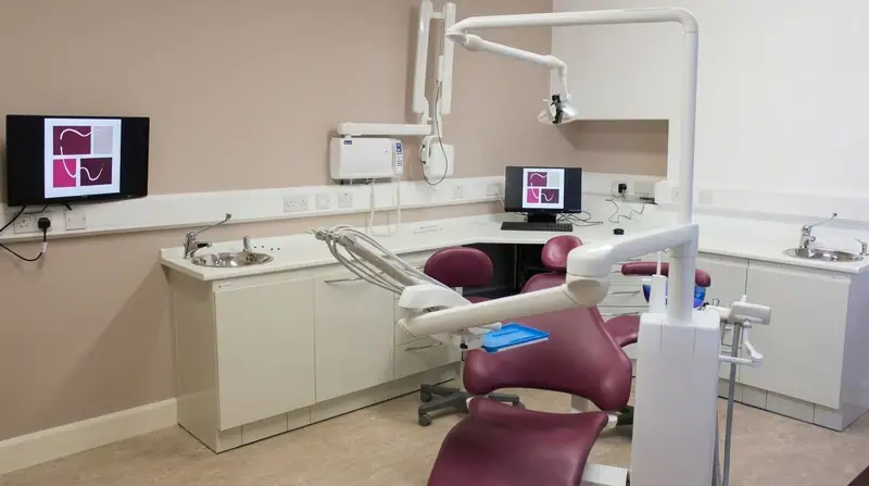 A treatment room with a burgundy chair and screens